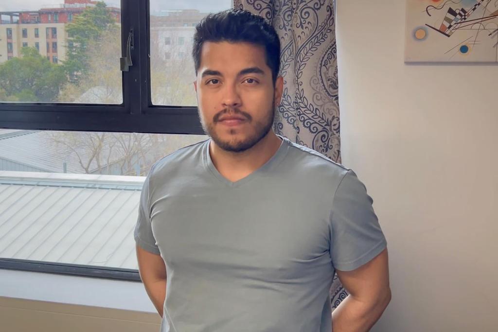 Man smirking with blue shirt next to window